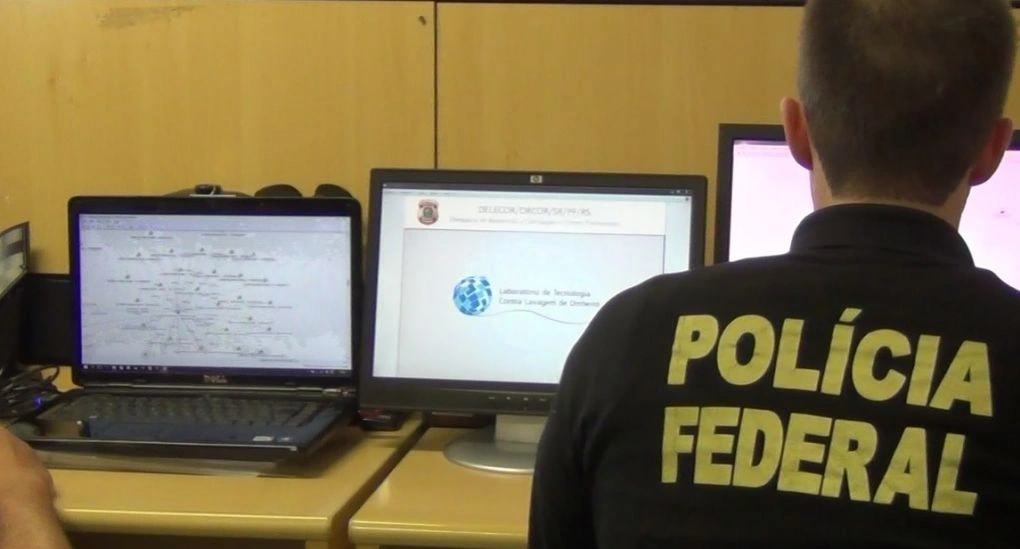 imagem de um policial trabalhando em frente ao computador na área administrativa da polícia federal